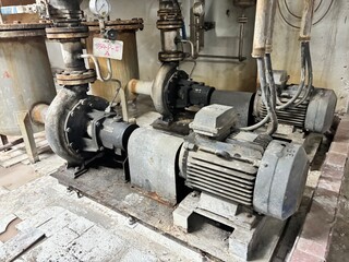 dirty industrial electric motor and an intricate web of pipes and valves. The scene conveys the...