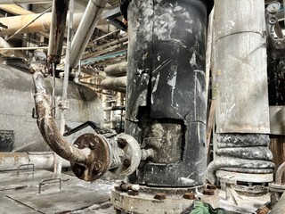 A row of large industrial insulated pipes with blue manual control valves inside an old factory,...