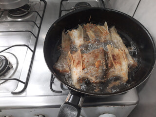 Fried fish in a pan on a gas stove, top view