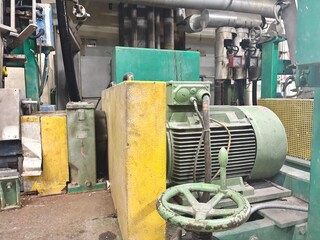 a heavy-duty industrial electric motor and an interconnected system of machinery and pipes. The equipment is painted green and yellow, giving it a weathered, operational appearance in a factory or wor