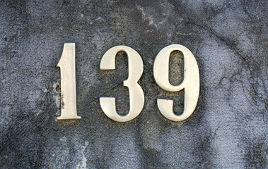House number 139 in metallic style mounted on a weathered concrete wall. Classic silver numerals...