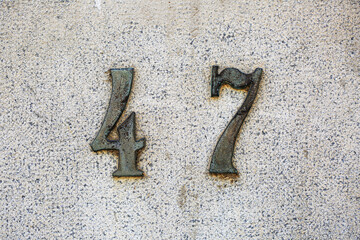 House number 47 in aged bronze style mounted on a textured stone wall. Rustic numerals with patina...