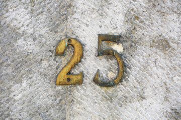 Vintage brass house number 25 mounted on a textured stone wall. Weathered metallic numerals with...