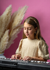 Little cute girl playing a keyboard, focused on keyboard, against soft pink background. Studio...