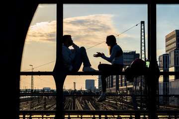 Par de amigos conversando sentados en las estructuras de una vieja estación de trenes, al atardecer