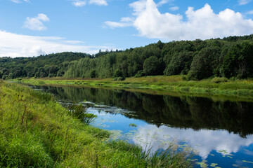Wide calm river in Russia with forested banks and cloudy summer sky. Peaceful rural scene with...
