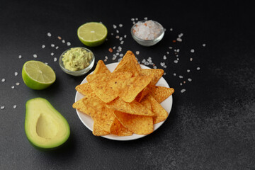 Plate of nacho chips with guacamole, lime, avocado and salt on dark background