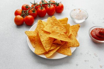 Plate of nacho chips with tomatoes, salt and dip on white background