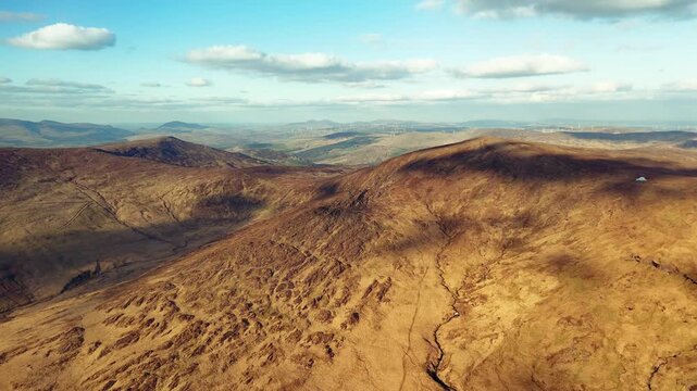 A scenic look at the mountainous terrain around Priest's Leap in County Cork, Ireland. Wind turbines are visible on the horizon, providing a distant contrast to the natural landscape.