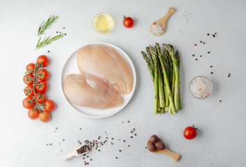 Raw chicken breast on white plate with vegetables and spices on table