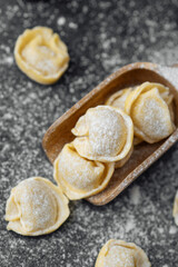 Wooden scoop with flour covered raw cappelletti pasta on dark background
