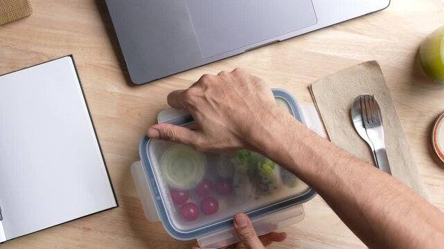 Top view of person eating Salad Wrap meal prep container on the office desk.