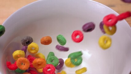 
Close up shot of multi colored cereal rings falling down in slow motion a pristine white bowl on the table - Powered by Adobe