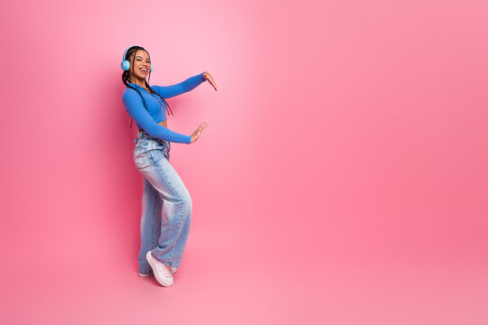 Smiling young woman with headphones in a trendy casual outfit enjoying music against a bright pink background