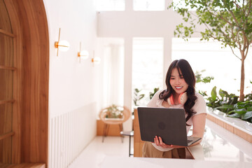Asian adult woman freelancer remote work laptop modern cafe productive professional happy digital...