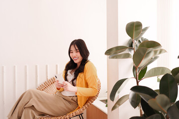 Asian adult woman happily uses smartphone for social media or remote work in a bright modern cafe...