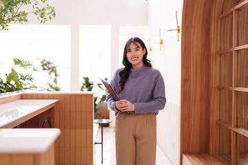 Asian Adult Woman Professional Standing Modern Cafe Interior Holding Clipboard Smiling Welcoming...