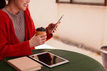 Asian adult woman uses smartphone drinks coffee works remote at outdoor cafe freelance lifestyle...