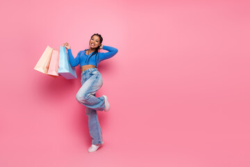 Happy young woman holding shopping bags wearing casual fashion outfit against pink background