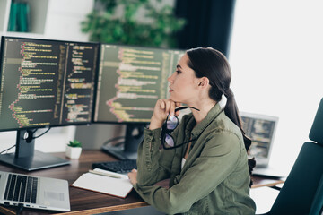 Focused woman programmer analyzing computer code on multiple monitors in a modern home office setting