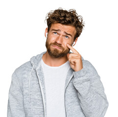 A confused man is trying to insert Bluetooth earphones while looking up, isolated on a transparent background.