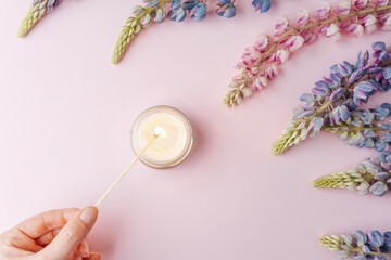 Hand lighting candle with lupine flowers on pink background