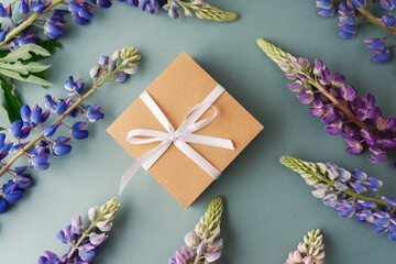Gift box with ribbon and lupine flowers on green background