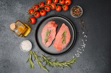 Raw veal steaks on black ceramic plate with rosemary cherry tomatoes salt oil and pepper