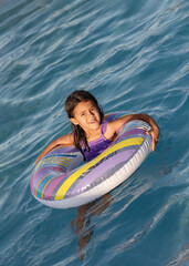 Little child girl in purple swimsuit swimming in the pool during summer vacation