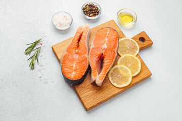 Fresh salmon fillets with lemon slices and seasoning on a wooden cutting board