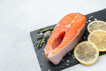 Fresh salmon fillet with lemon slices and herbs on a dark slate board