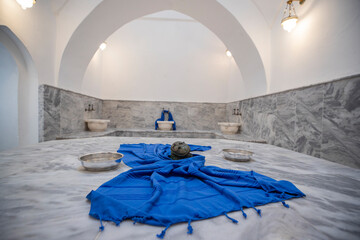 
Traditional Turkish Hammam Interior with Marble Platform, Blue Towel and Copper Bowls
