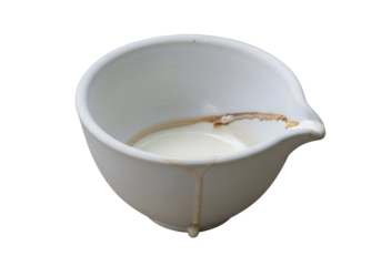 Close-up of a white ceramic creamer with coffee stain marks and a spout on a black background