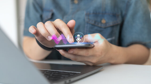 Person using smartphone with hologram microphone and soundwave icons, representing voice recognition, speech to text, and AI assistant technology.