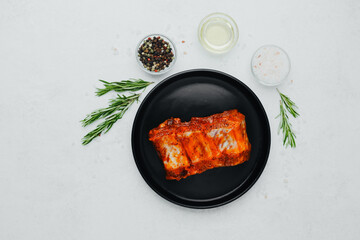 Spicy pork ribs on black plate with seasoning and herbs