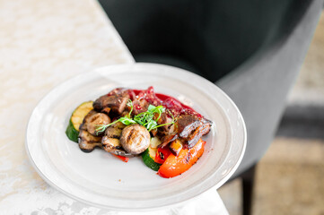 Grilled vegetables with mushrooms, zucchini, and bell peppers garnished with microgreens on a white plate, served on a light tablecloth.