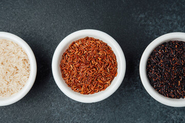Three types of rice in bowls on dark background top view