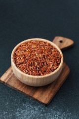 Red rice in wooden bowl placed on cutting board over dark surface