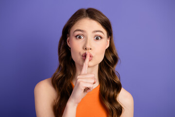 Portrait of beautiful young woman gesturing shh with lips on purple background, wearing trendy...