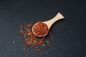 Wooden spoon filled with red rice and scattered grains on black background