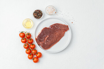 Raw beef steak on white plate with tomatoes and cooking ingredients