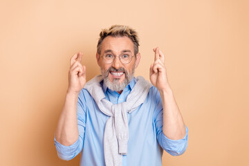 Bearded senior businessman with crossed fingers expressing hope and positivity in stylish attire...