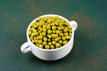 Green peas in white bowl on rustic dark background for vegan, vegetable or healthy ingredient concept