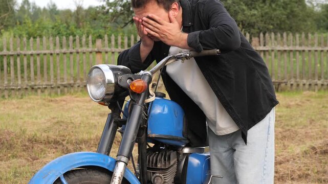 Frustrated motorcyclist covering face with hands leaning on broken motorcycle