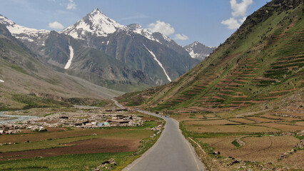 Mountain valley with winding road and snow patches
