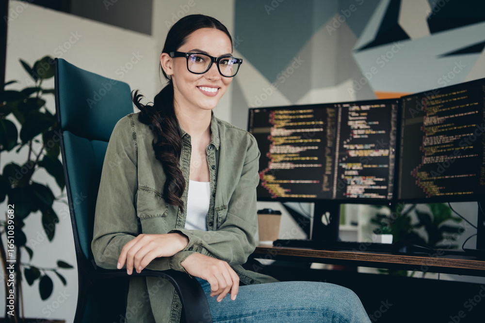 Poster young female programmer working in a modern office setting with monitors displaying code, showcasing