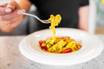 Close-up of tagliatelle pasta with creamy yellow sauce, cherry tomatoes, and herbs on a white...