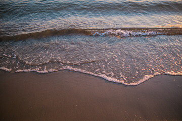 Gentle ocean wave lapping sandy beach at sunset