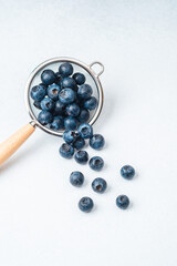Fresh blueberries in a strainer with some spilling out on a white surface