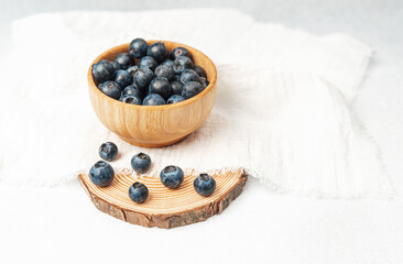 Fresh blueberries in wooden bowl on white fabric background